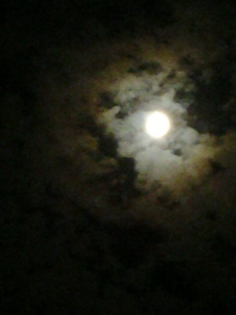 Full moon surrounded by dark, cloudy sky.