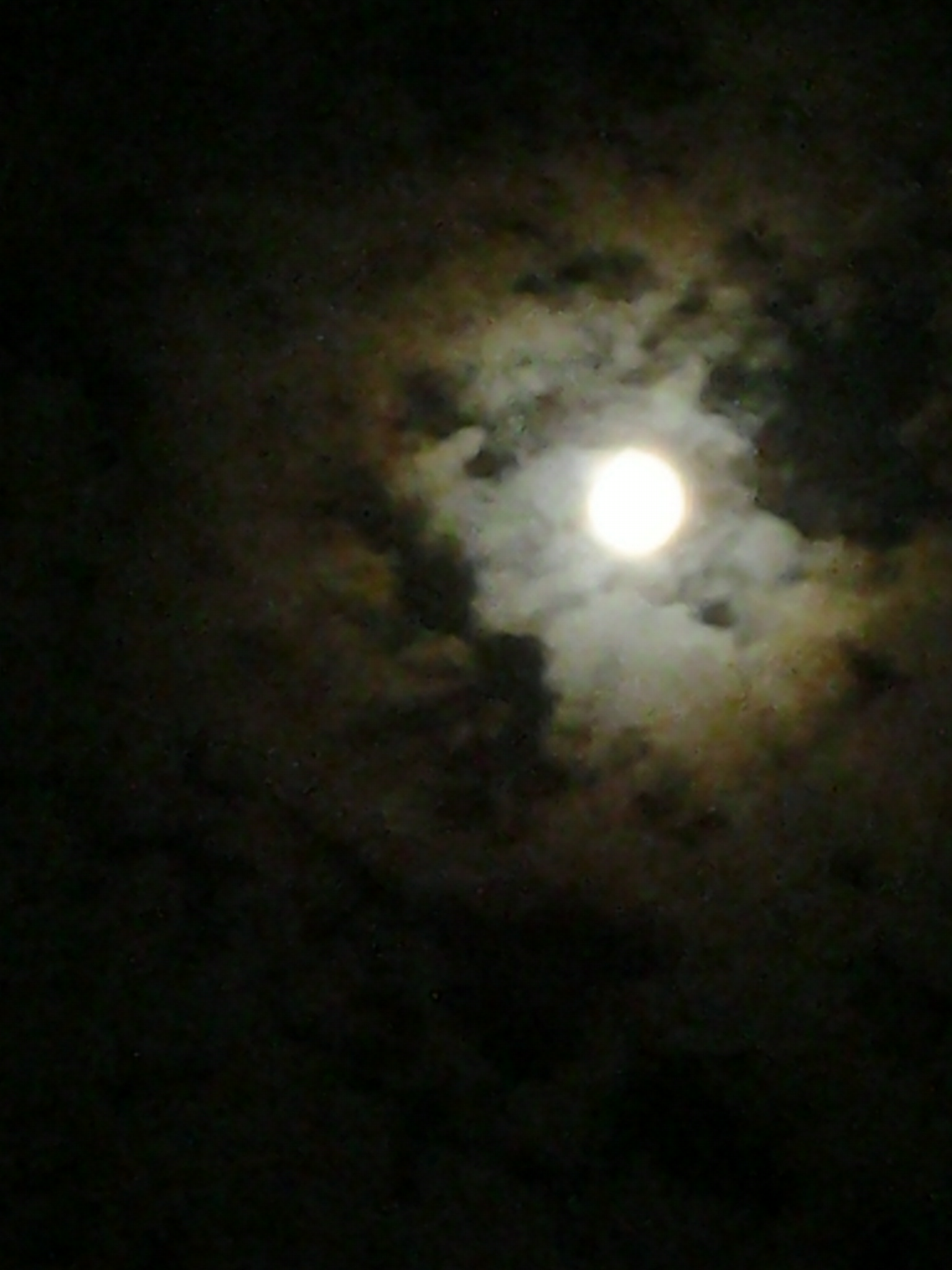 Full moon surrounded by dark, cloudy sky.