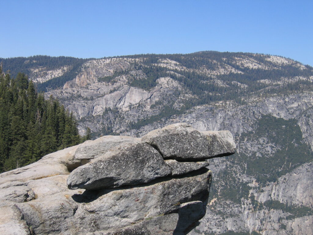 Rocky cliff overlooking mountainous landscape, clear sky.