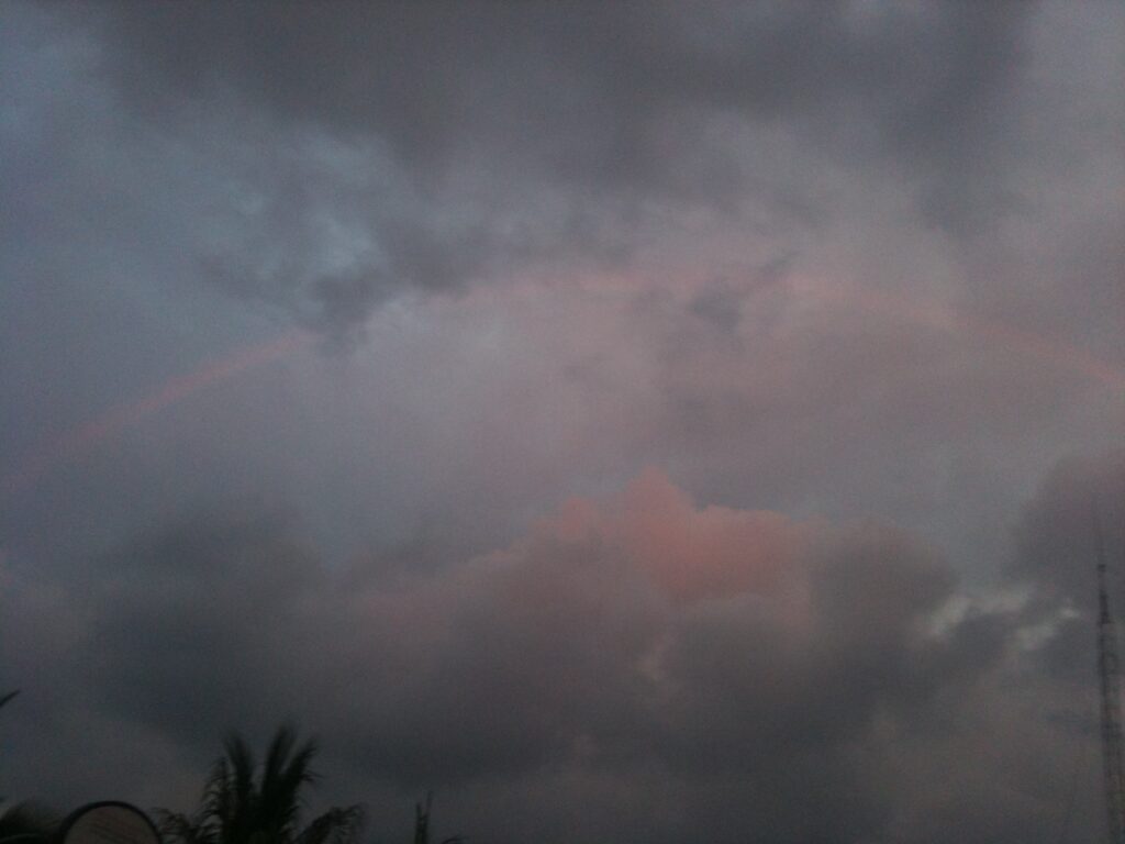 Faint rainbow in cloudy evening sky.
