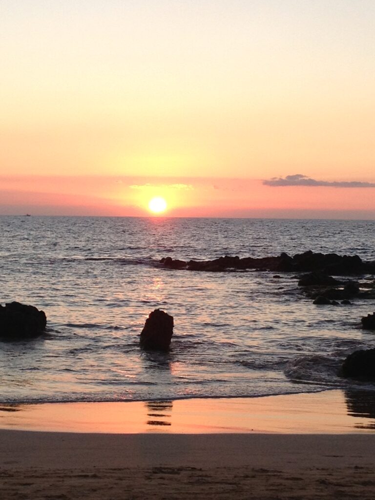 Sunset over ocean with rocky shoreline.