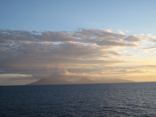 Distant island under cloudy sunset sky.