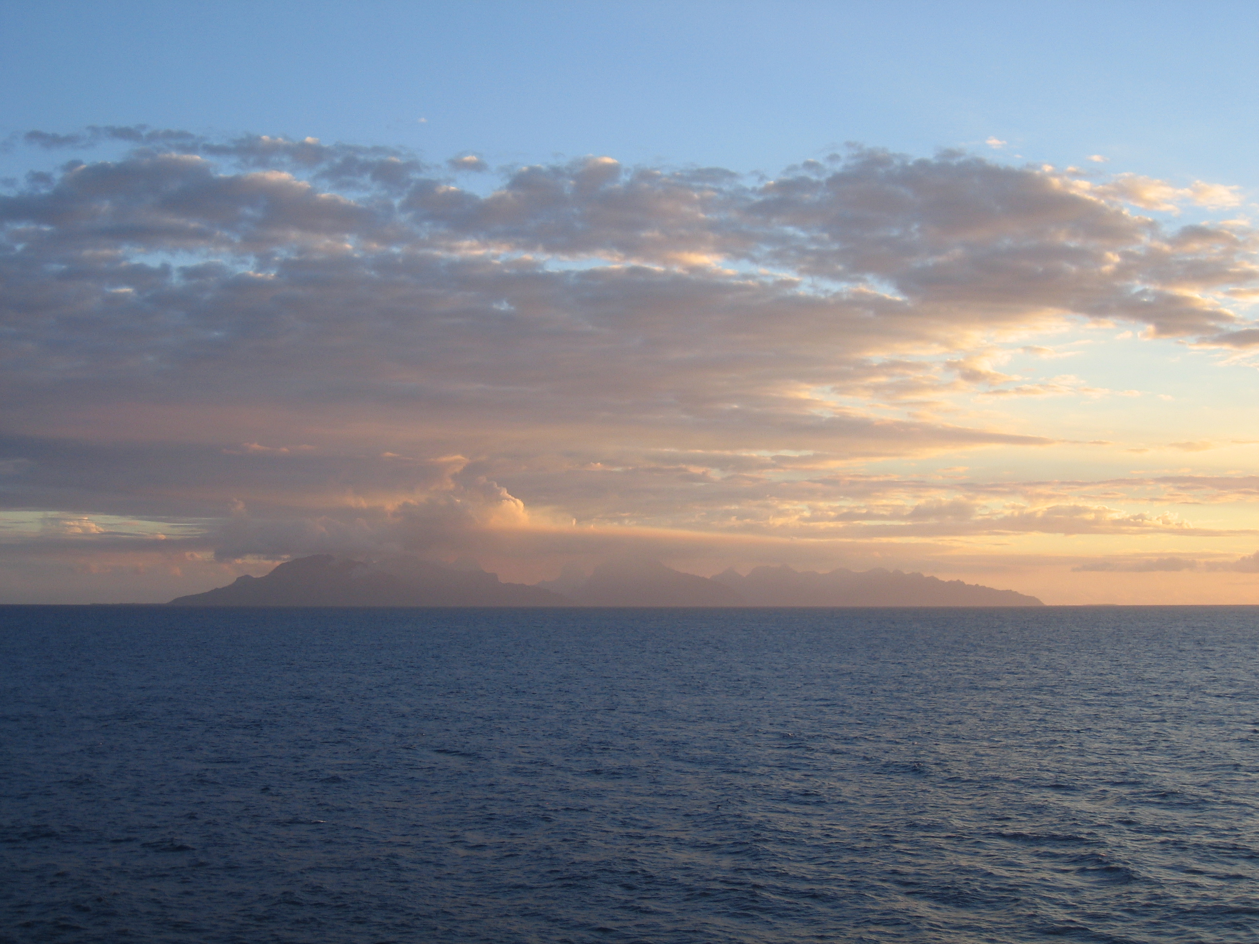 Distant island under cloudy sunrise sky.