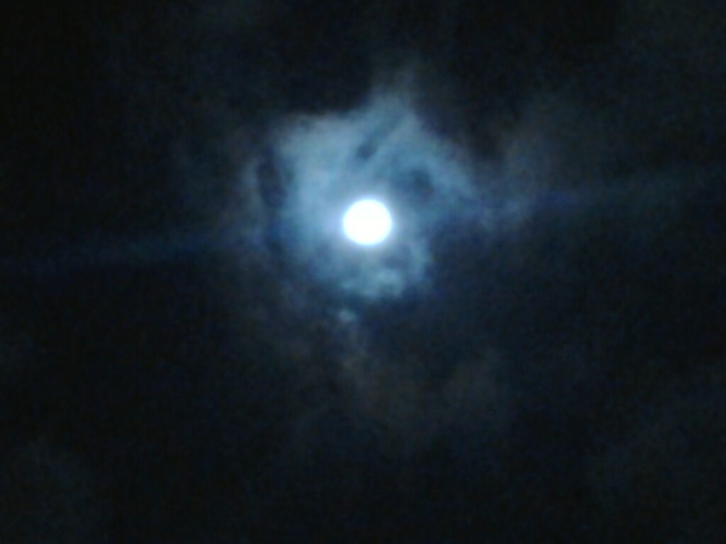 Moon shining through dark, cloudy night sky.