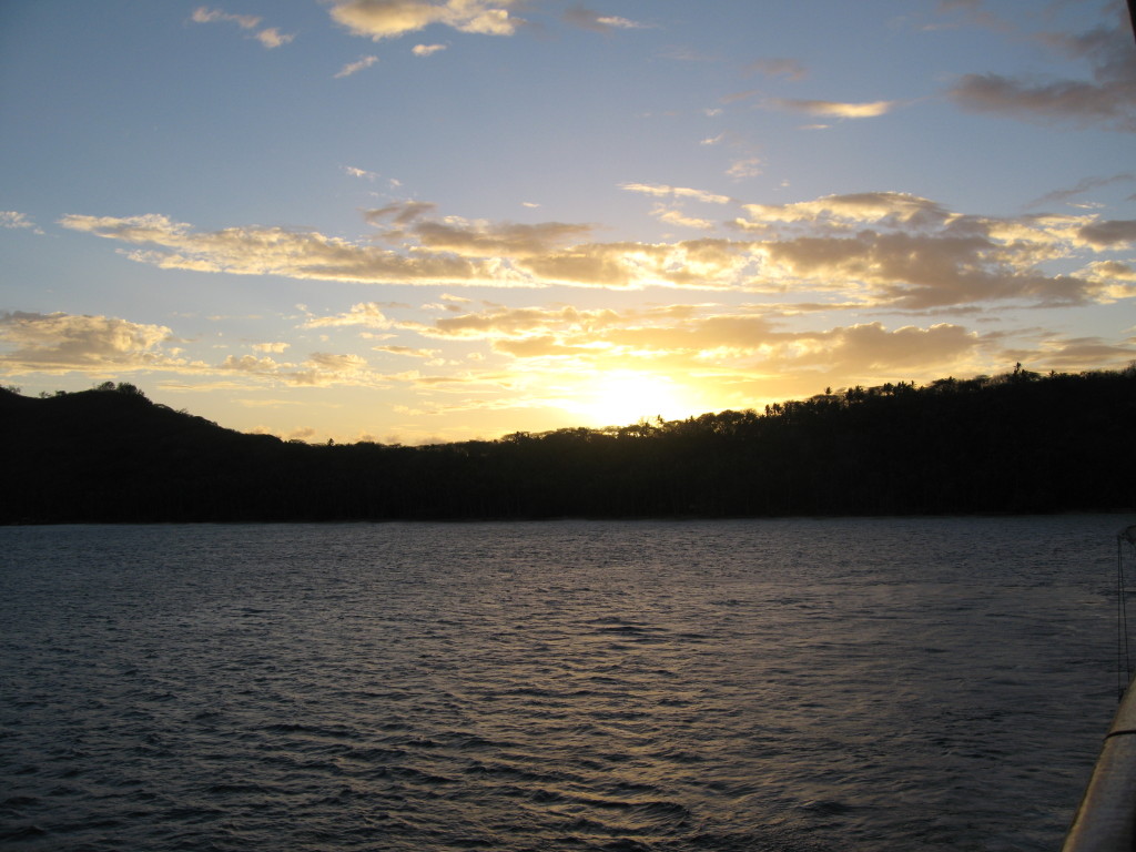 Sunset over calm lake and silhouetted hills.