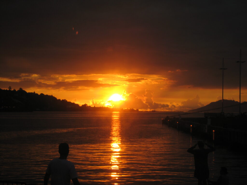 Sunset over calm water with silhouettes.