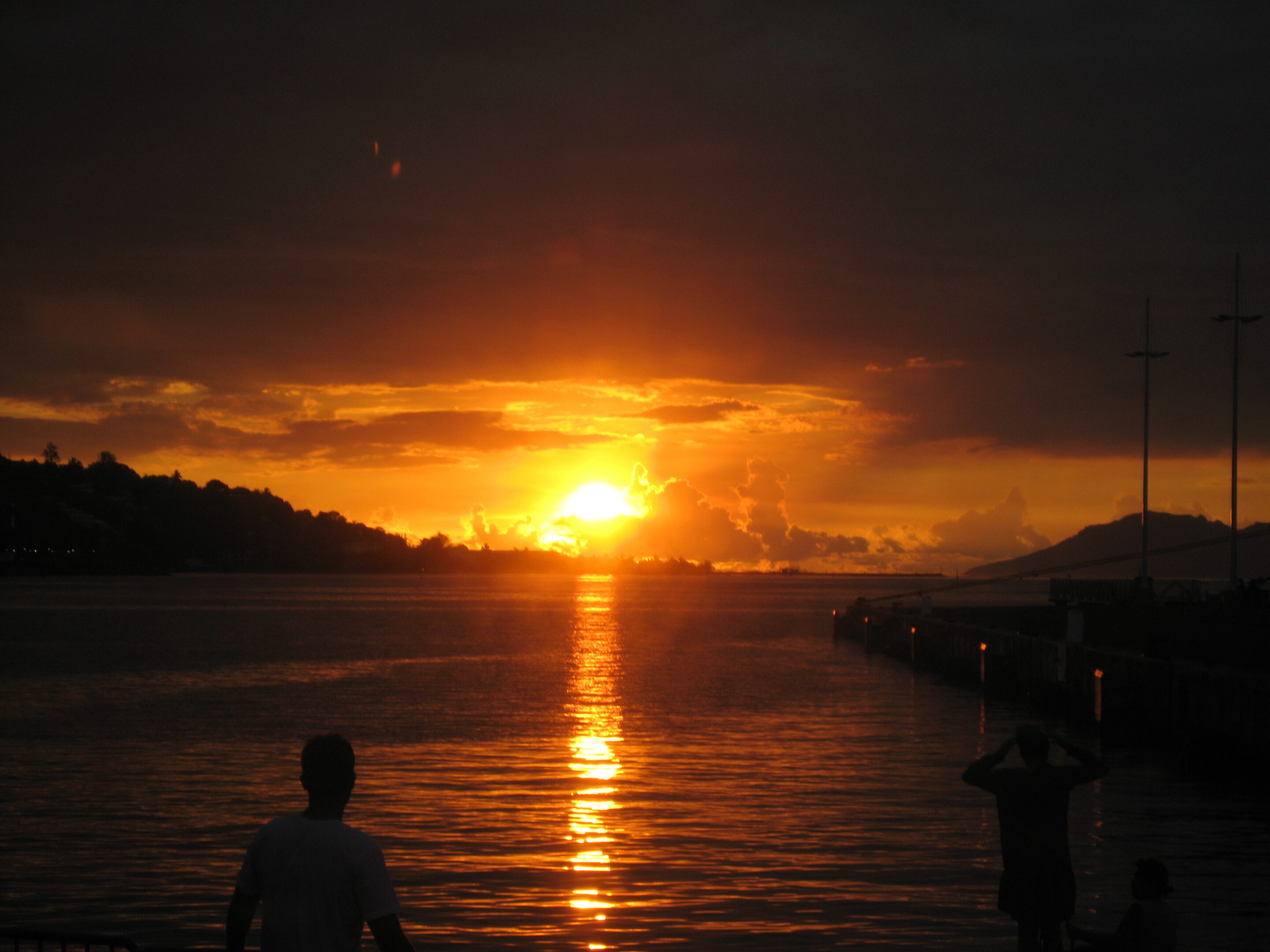 Sunset over calm water with silhouettes.