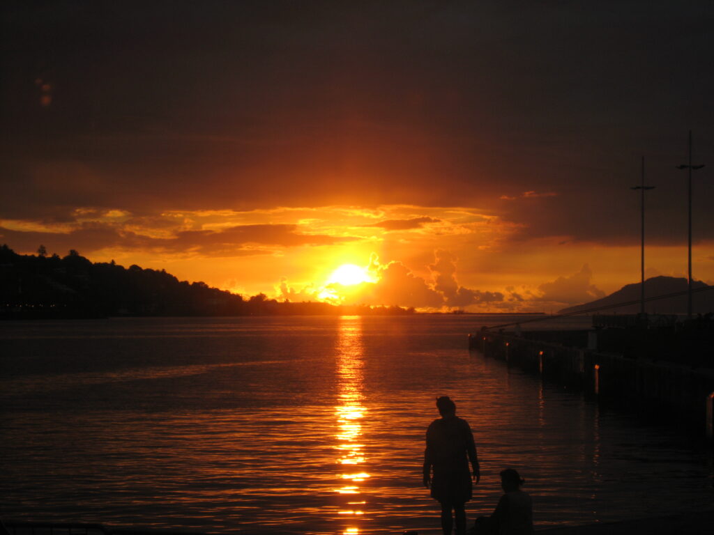 Sunset over water with silhouetted figures.