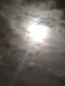 Bright moon behind cloudy night sky.