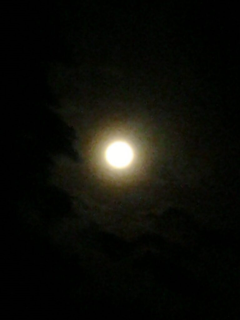 Full moon glowing in dark cloudy sky.