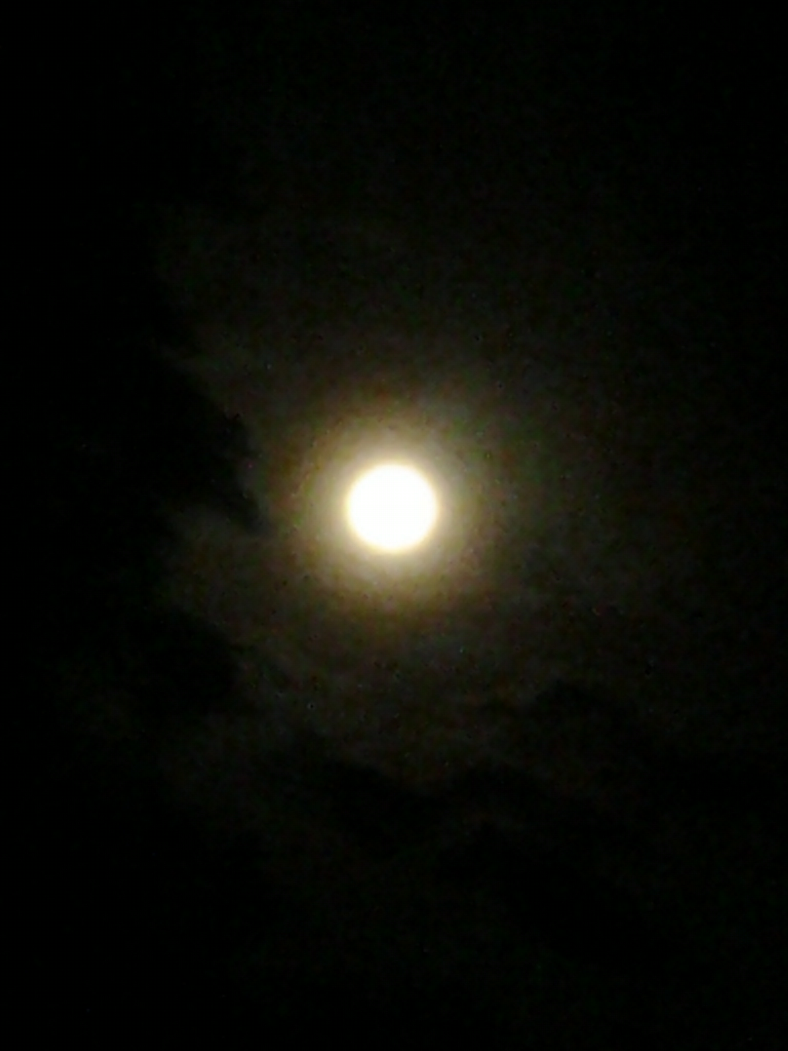 Full moon glowing in dark cloudy sky.