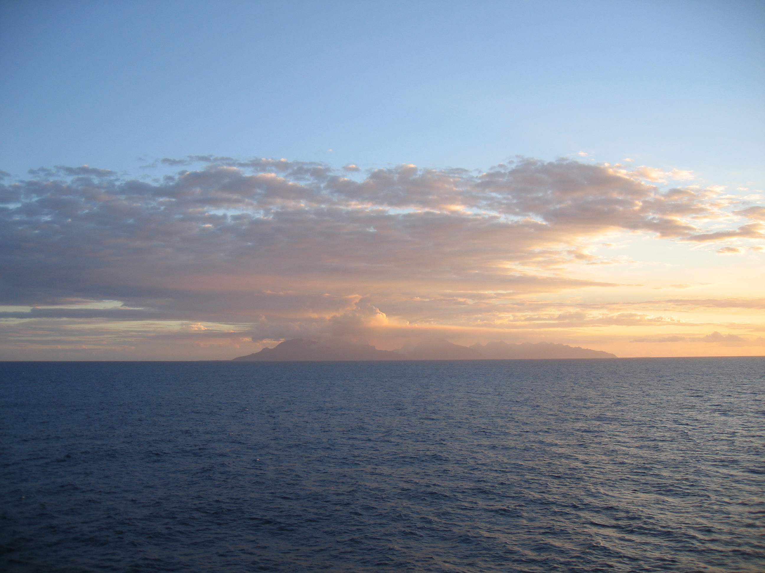 Ocean sunset with distant cloudy island view.