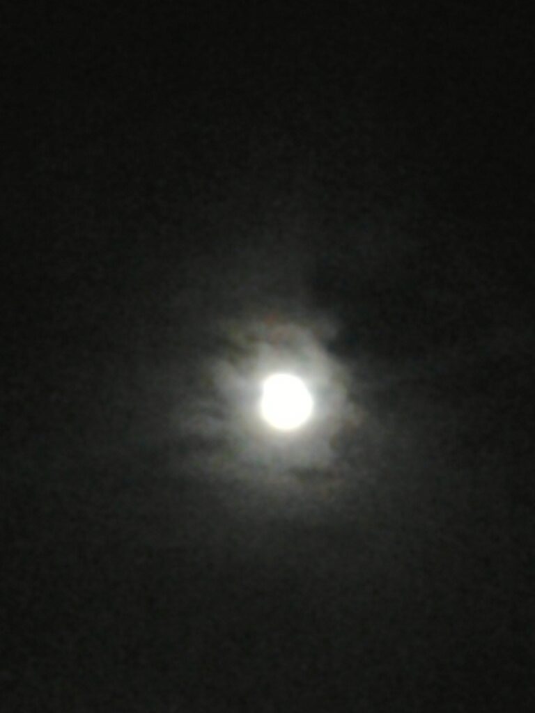 Full moon shining through cloudy night sky.