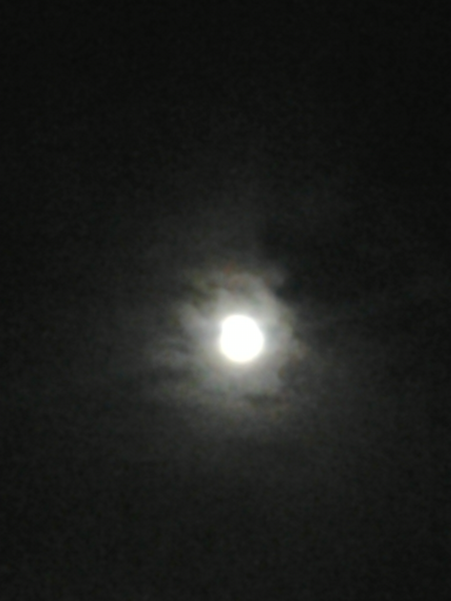 Full moon shining through cloudy night sky.