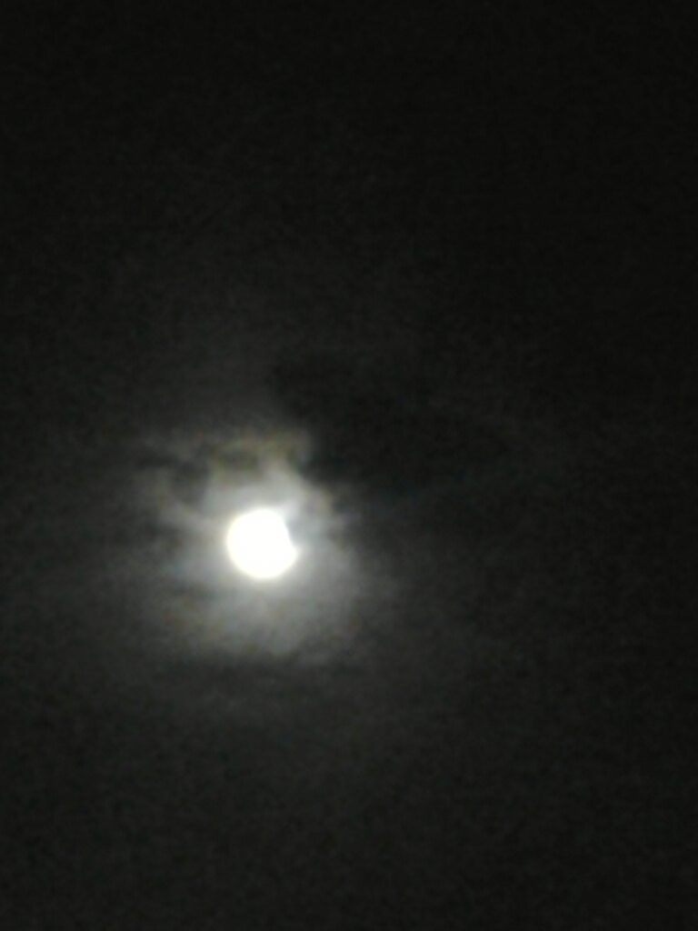 Full moon glowing through dark night clouds.