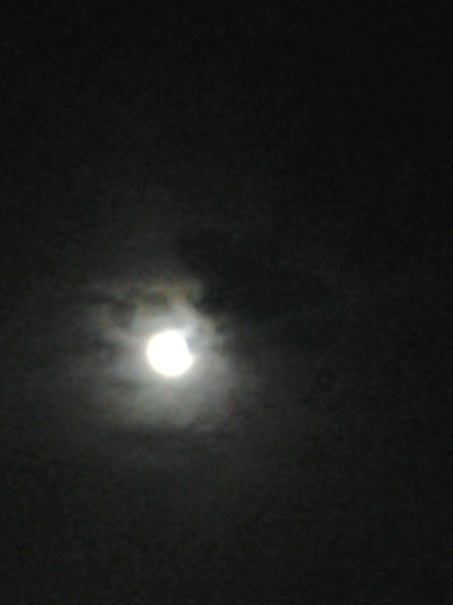Full moon glowing through dark night clouds.