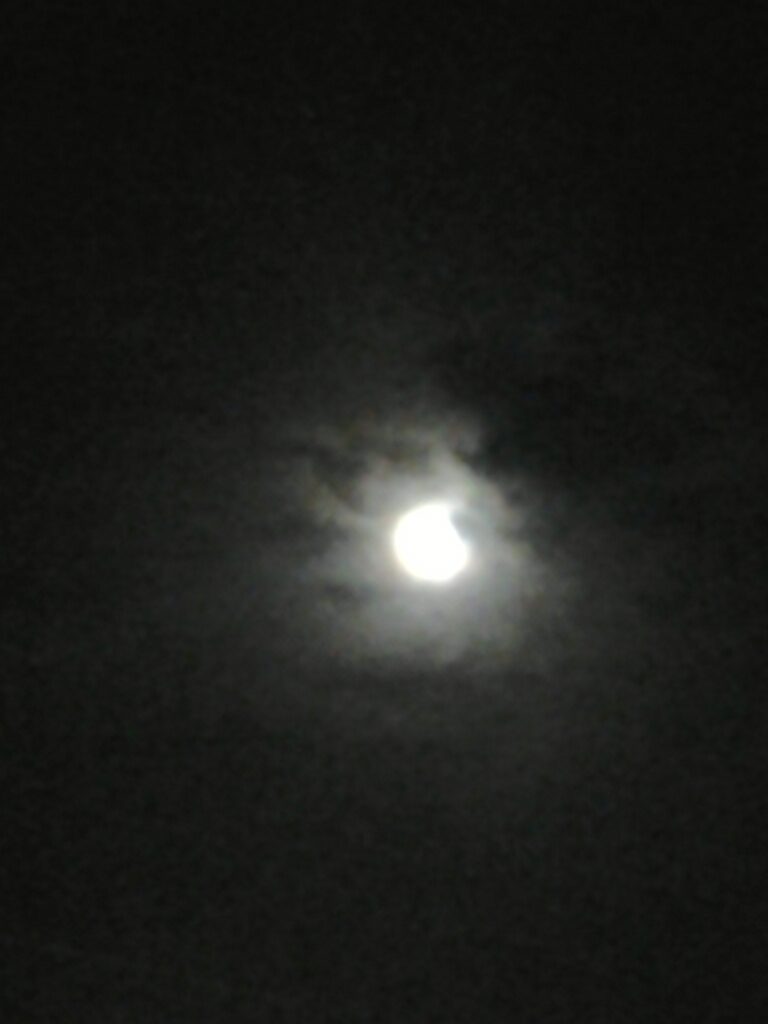 Moon obscured by clouds in night sky.