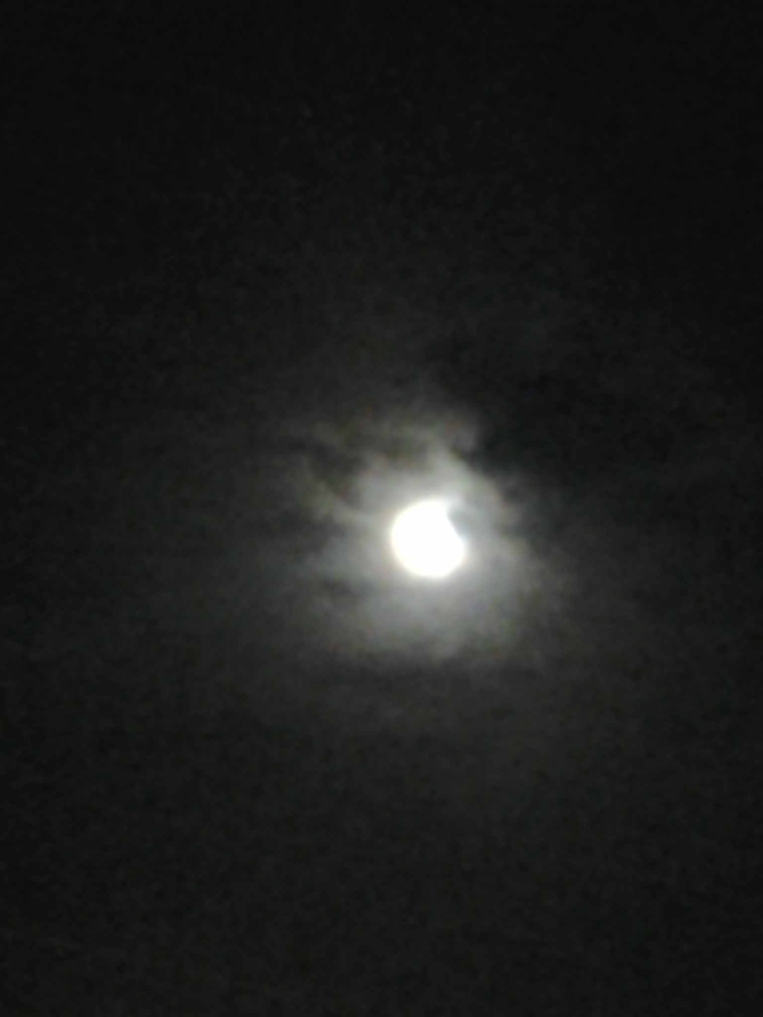 Moon obscured by clouds in night sky.