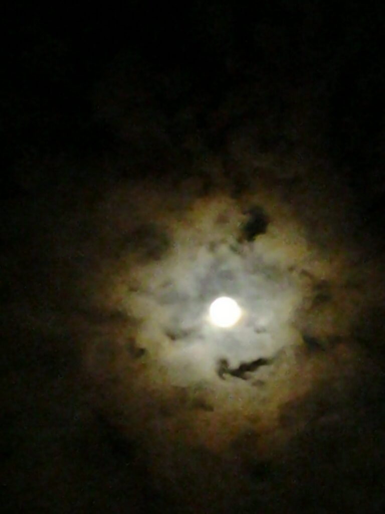 Full moon surrounded by dark, cloudy sky.