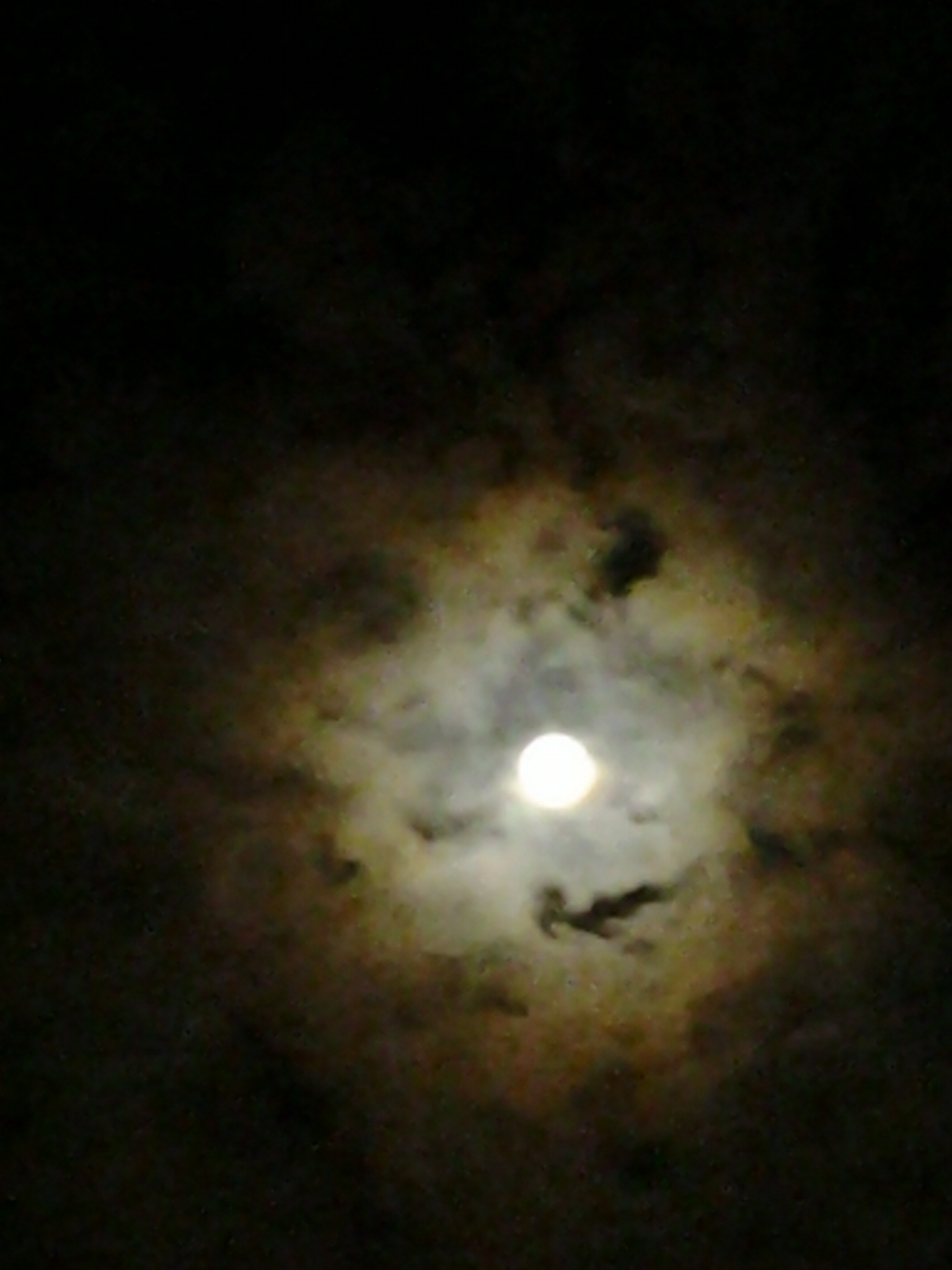 Full moon surrounded by dark, cloudy sky.