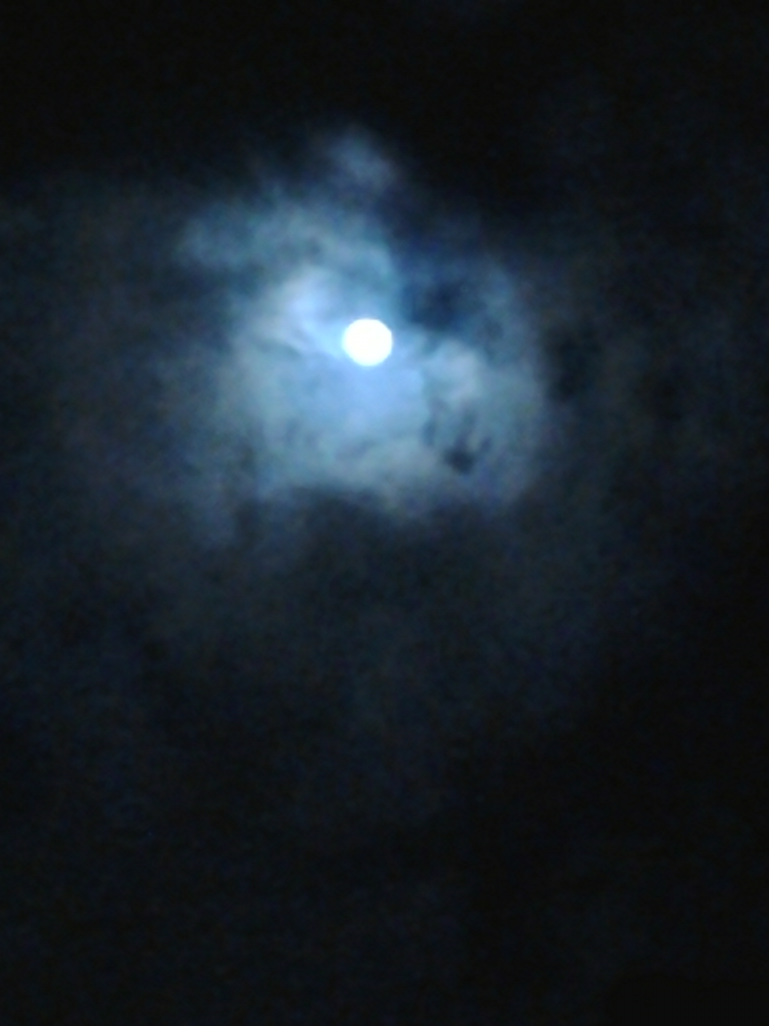 Moon shining through dark, cloudy sky.