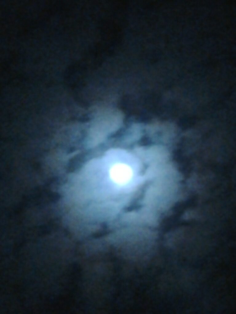 Moon shining through cloudy night sky.