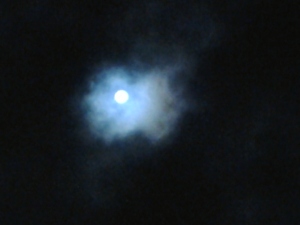 Moon shining through cloudy night sky.