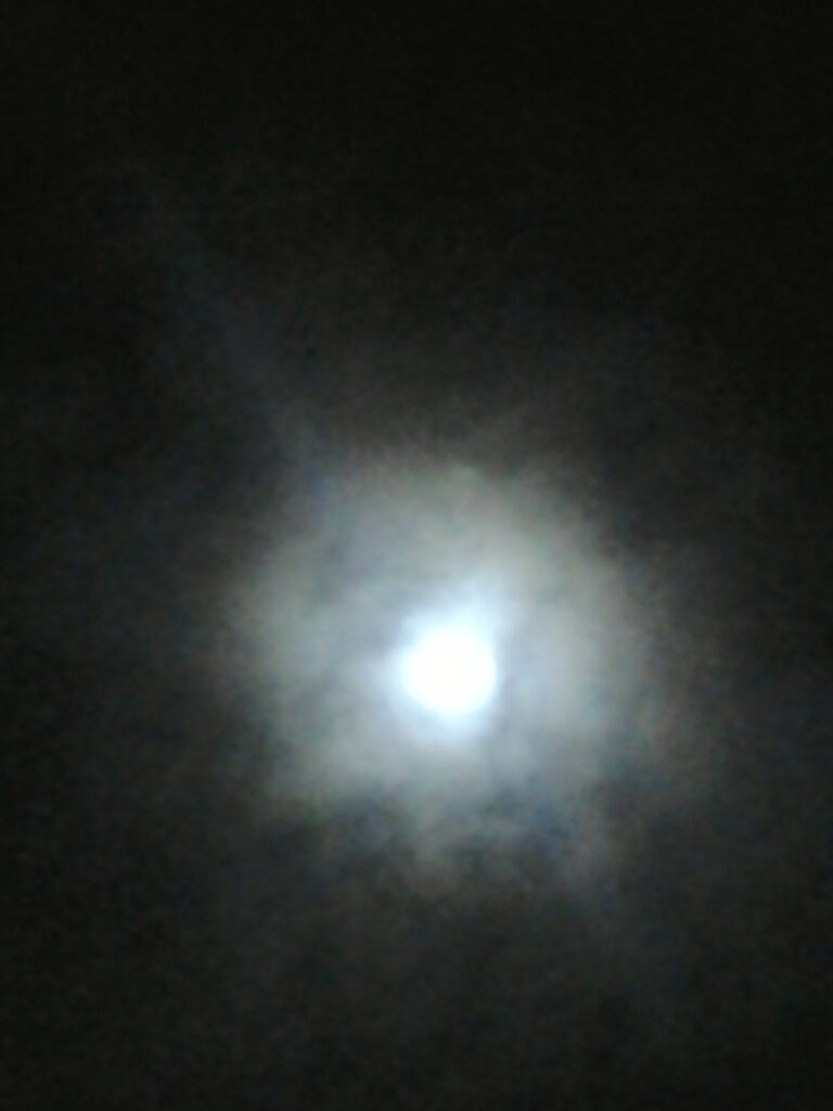 Bright full moon surrounded by cloudy haze.