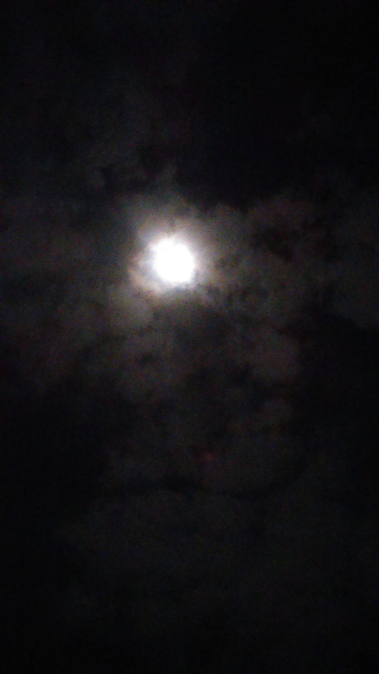 Moon shining through dark, cloudy night sky.