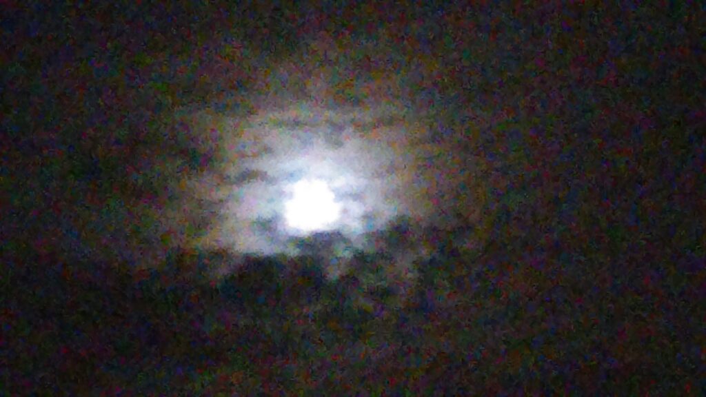 Full moon behind cloudy night sky.