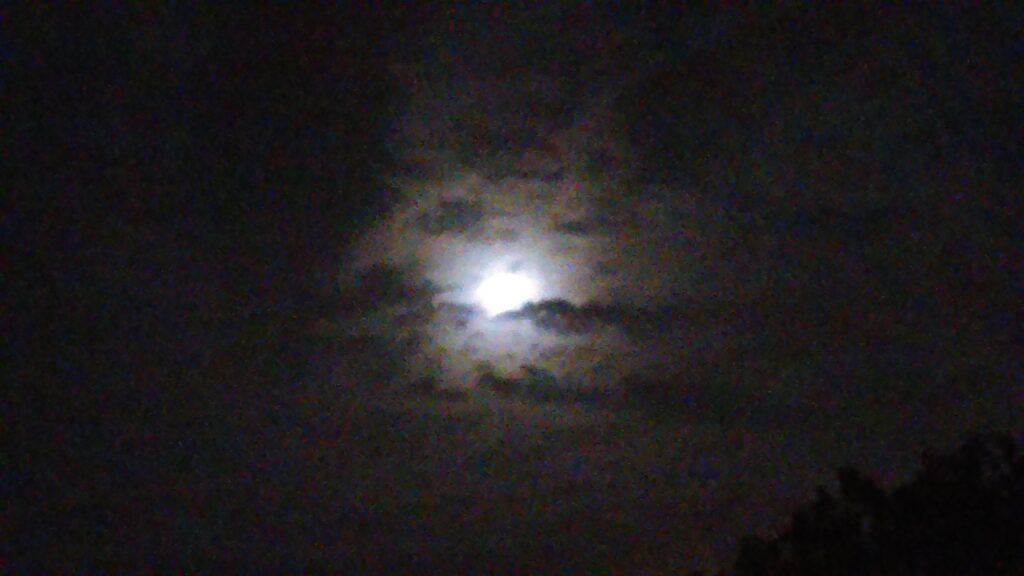 Full moon behind clouds at night.