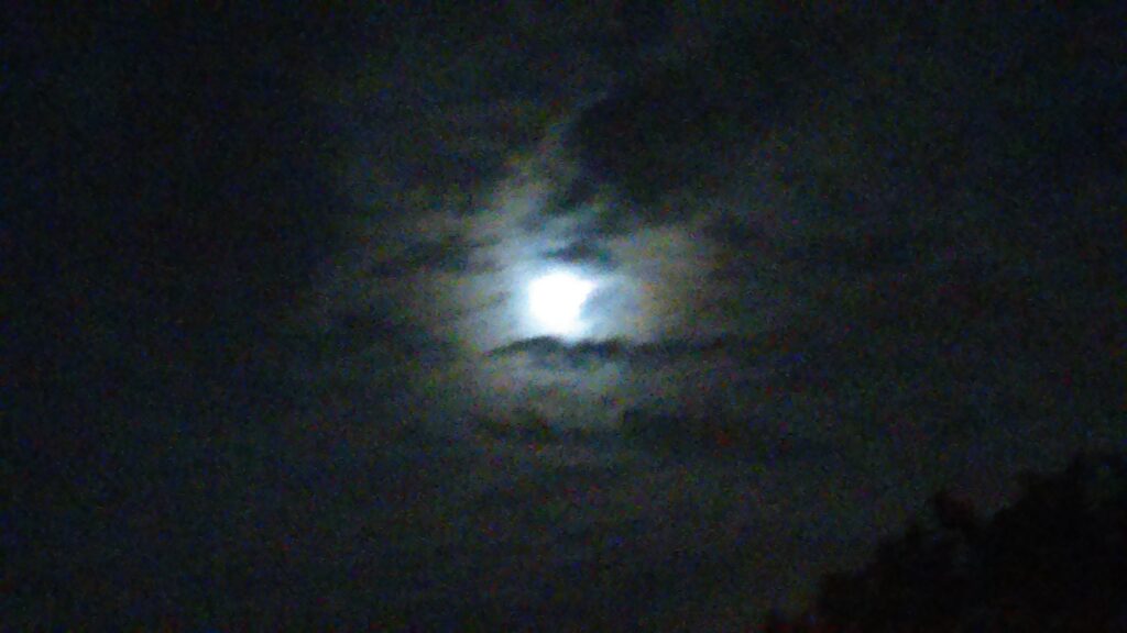 Moon shining through dark, cloudy night sky.