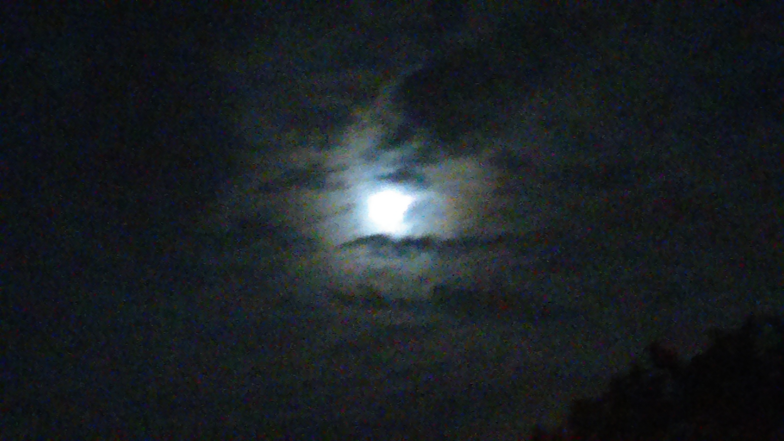 Moon shining through dark, cloudy night sky.