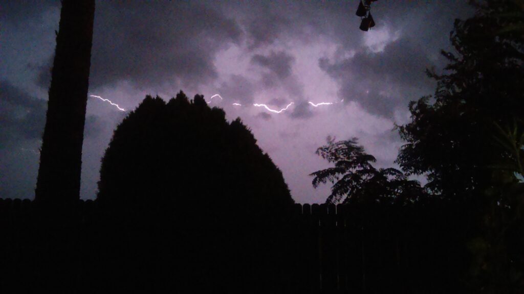 Lightning in the night sky over trees.