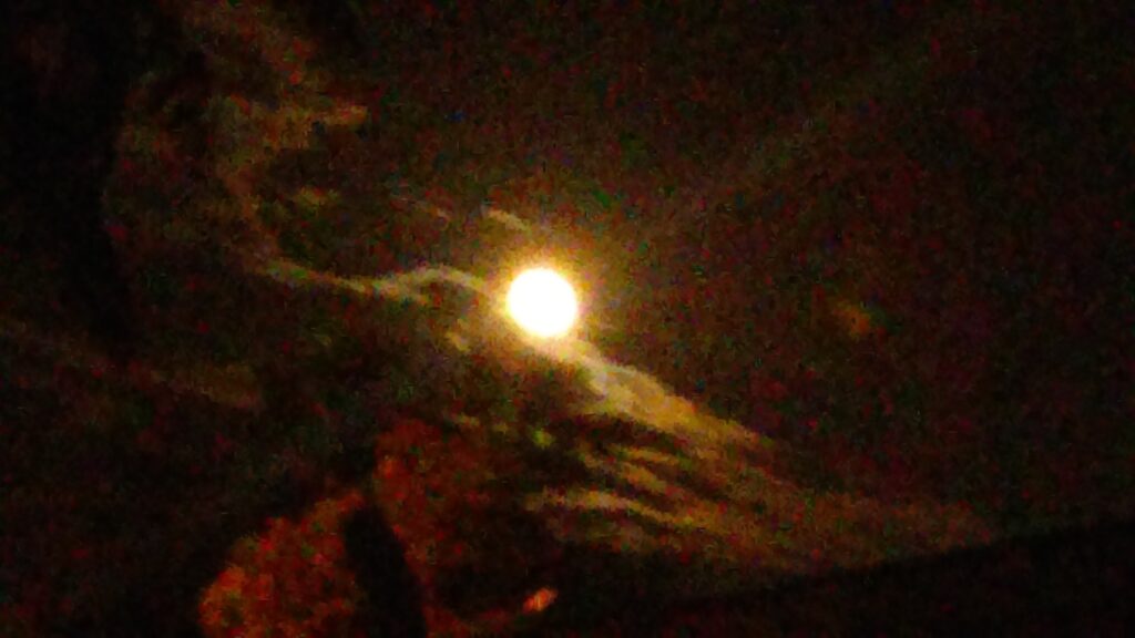 Bright moon obscured by dark clouds.
