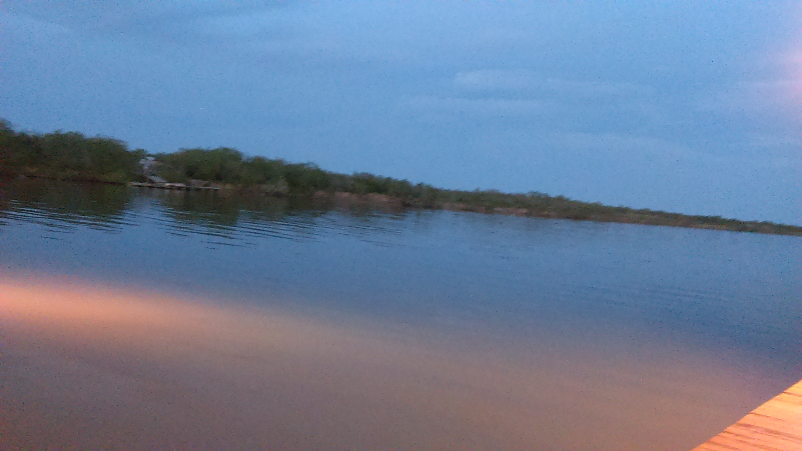 Calm lake at dusk with cloudy sky.