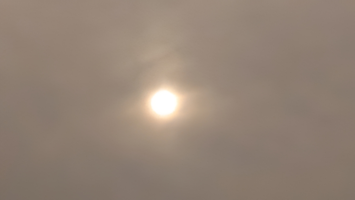 Sun obscured by hazy, cloudy sky.