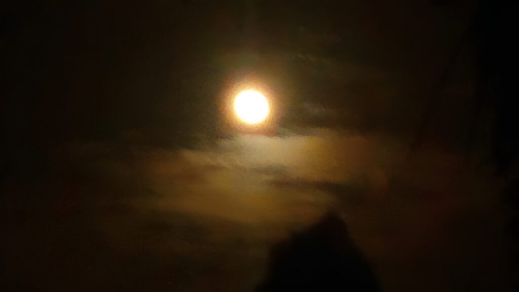 Full moon glowing through cloudy night sky