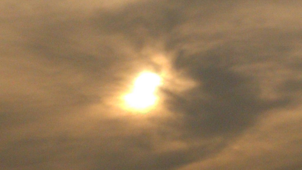Sun partially obscured by cloudy sky.