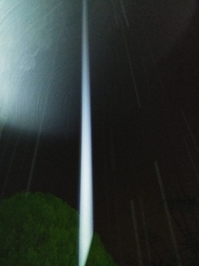 Tall light beam in dark night sky.