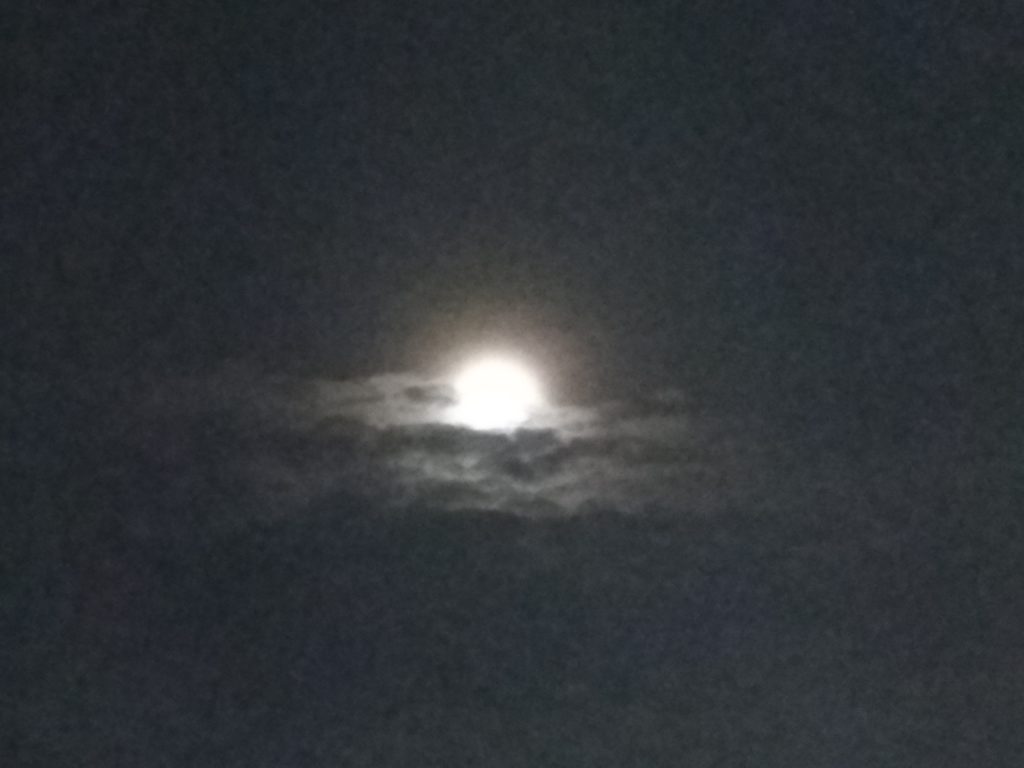 Full moon behind dark, cloudy sky.