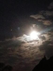 Bright moon shining through cloudy night sky.