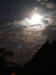 Bright moon shining through cloudy night sky.