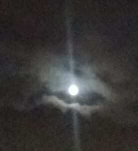 Bright moon shining through cloudy night sky.