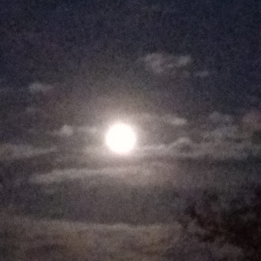 Full moon shining through cloudy night sky.
