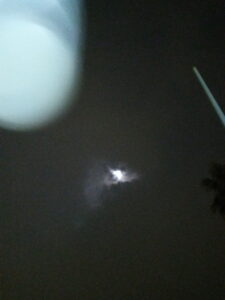 Moon in cloudy night sky, blurred foreground.