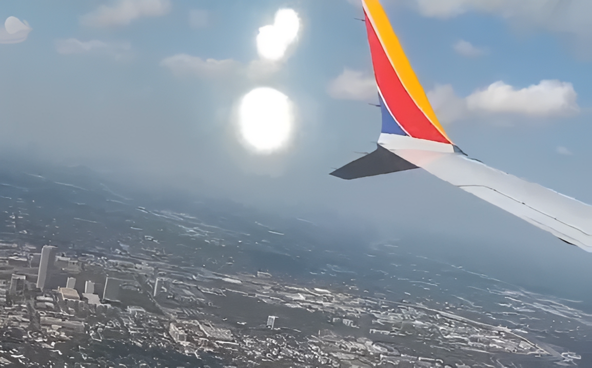 Airplane wing over cityscape with bright reflections.