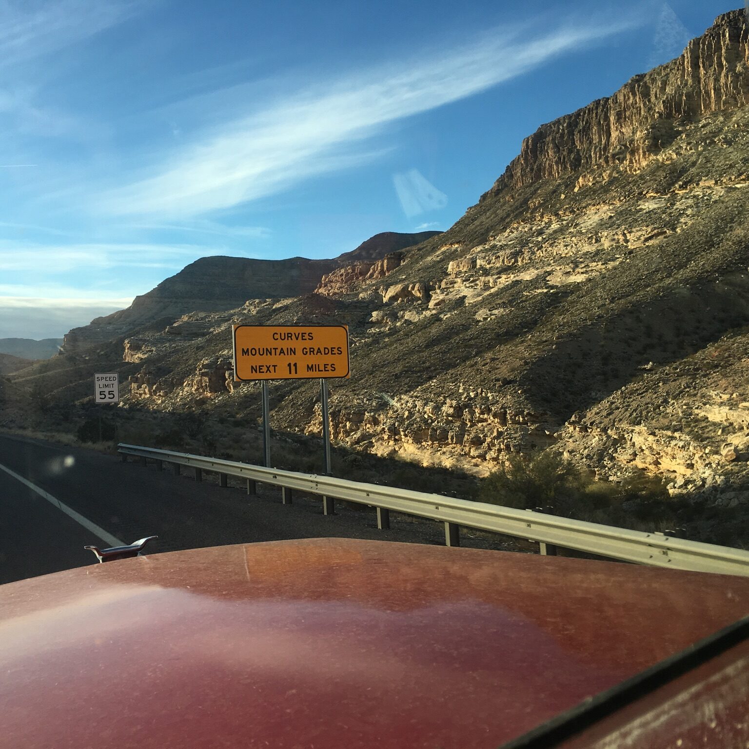 Mountain road with caution sign and cliffs.