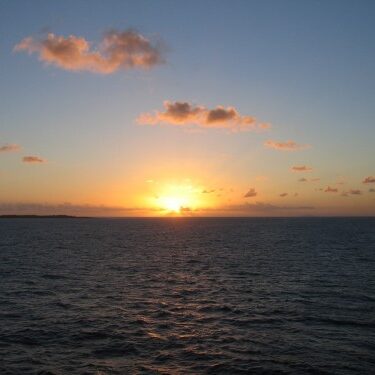 Sunset over the ocean with scattered clouds.