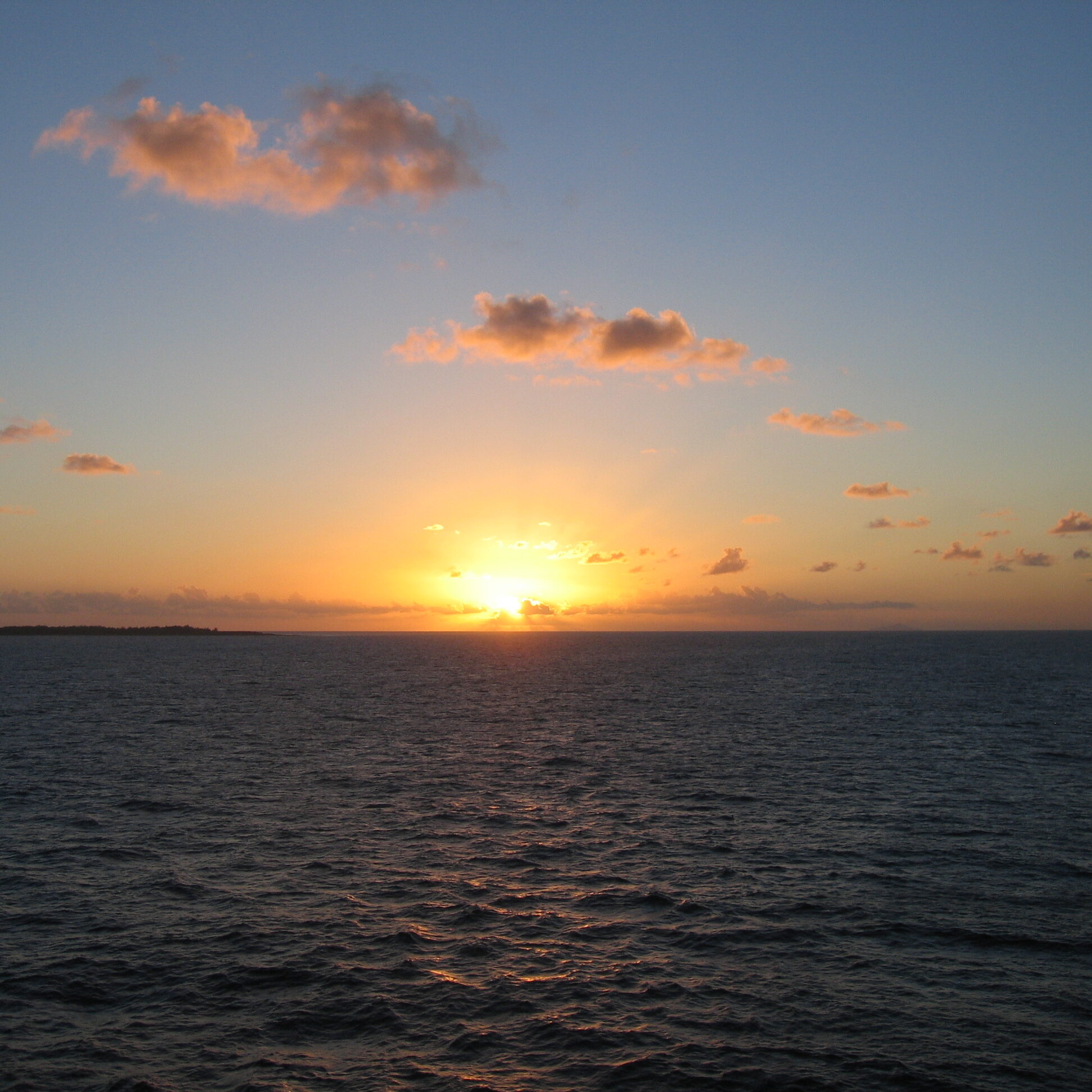 Sunset over the ocean with scattered clouds.
